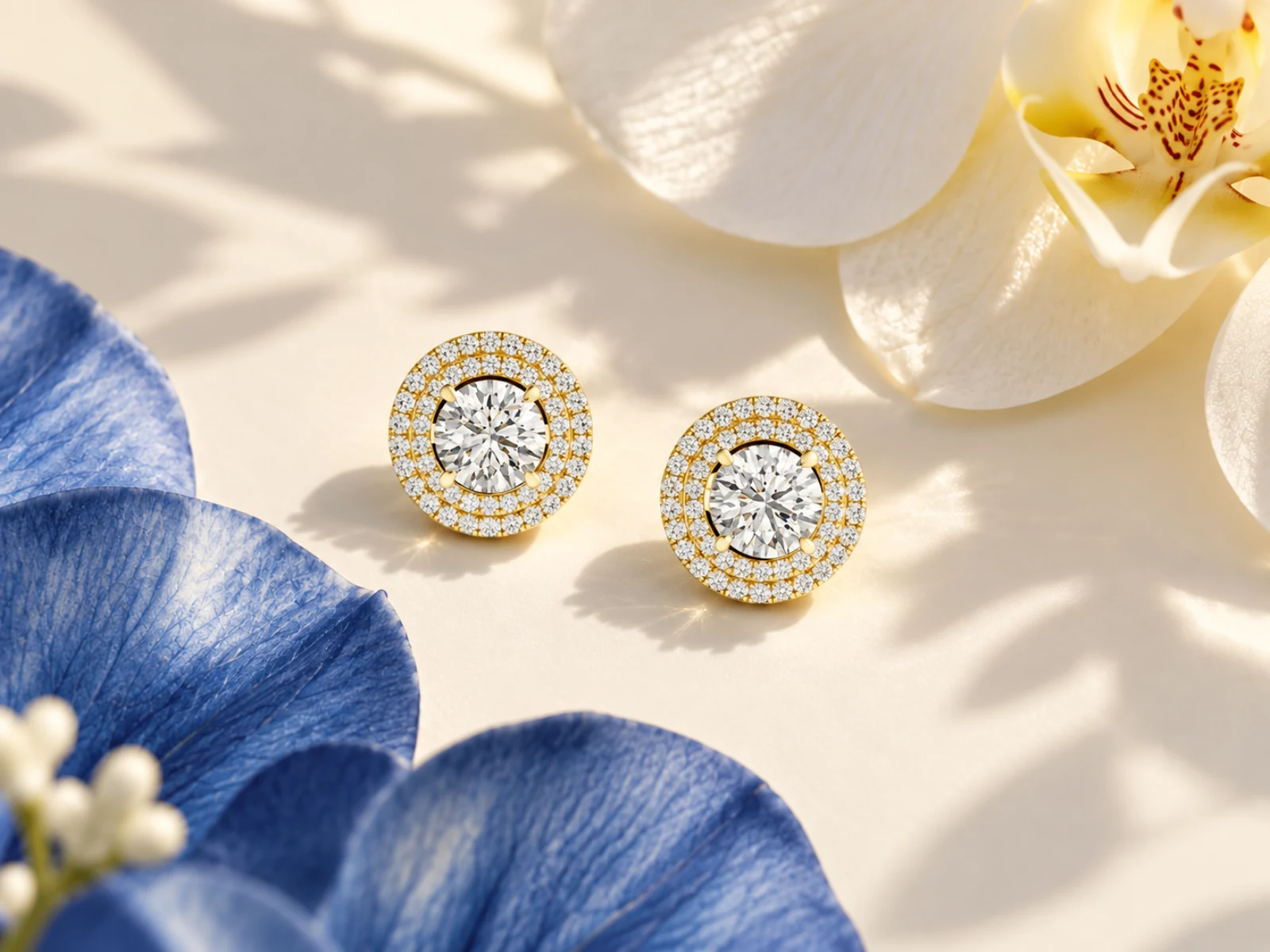 Angkor Relief Trace gold studs, No.08884, resting among ivory and blue orchids.